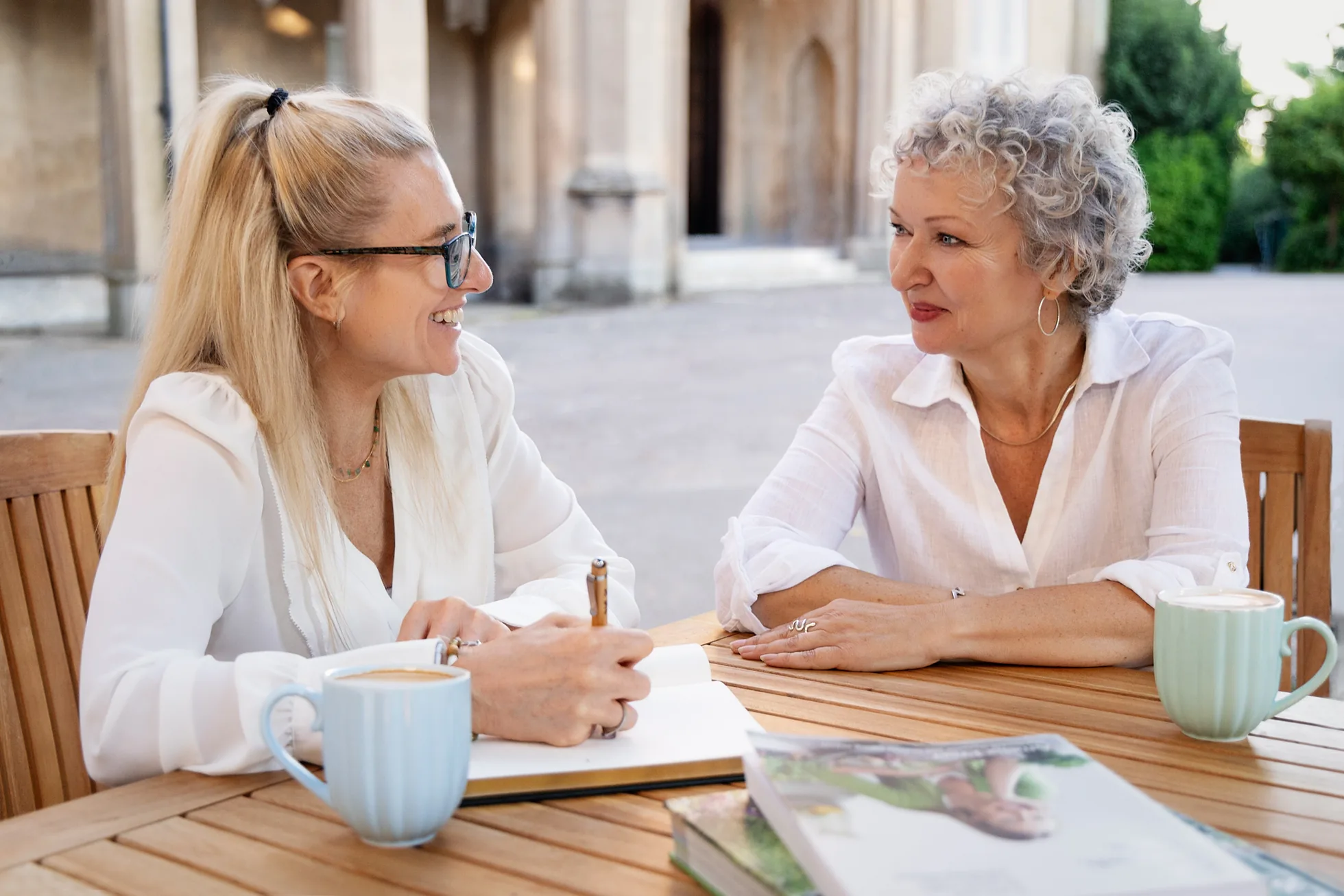 Charlotte Sinclair in conversation with an older woman at an outdoor table, both smiling.