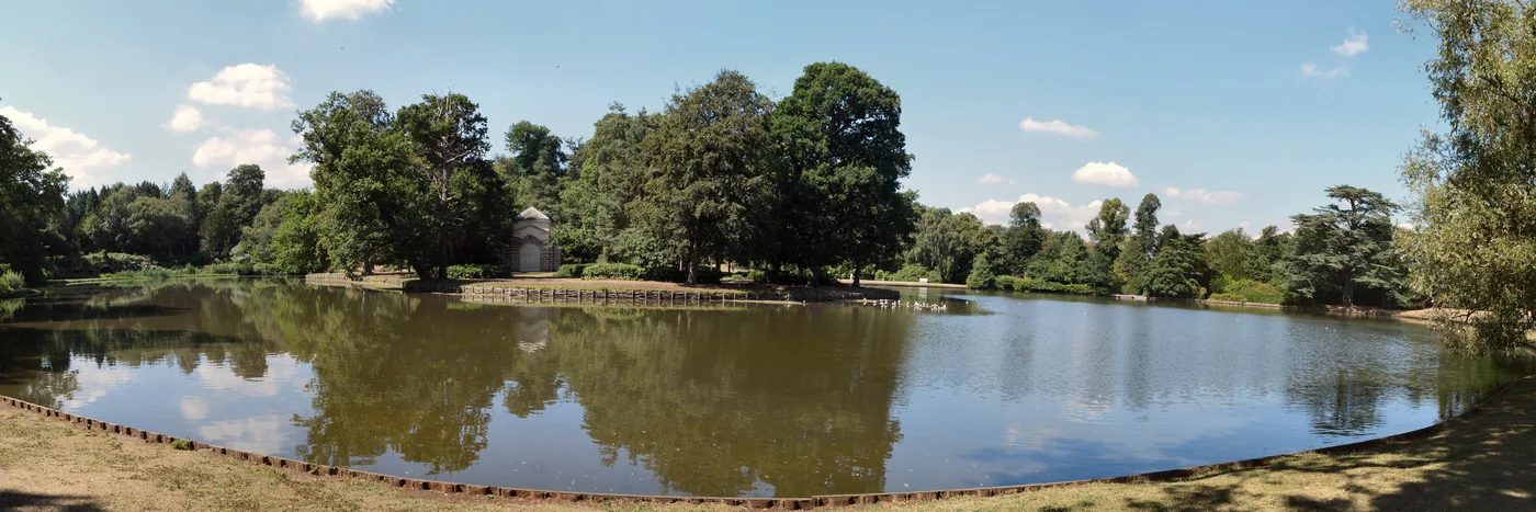 The lake at Claremont Landscape Garden in Esher, seen across the water towards the pavilion and the trees behind it.