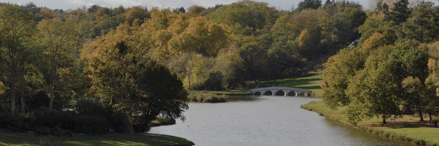 The lake at Painshill Park in Cobham seen from the Gothic Temple, the five-arch bridge crossing the water between autumn trees.