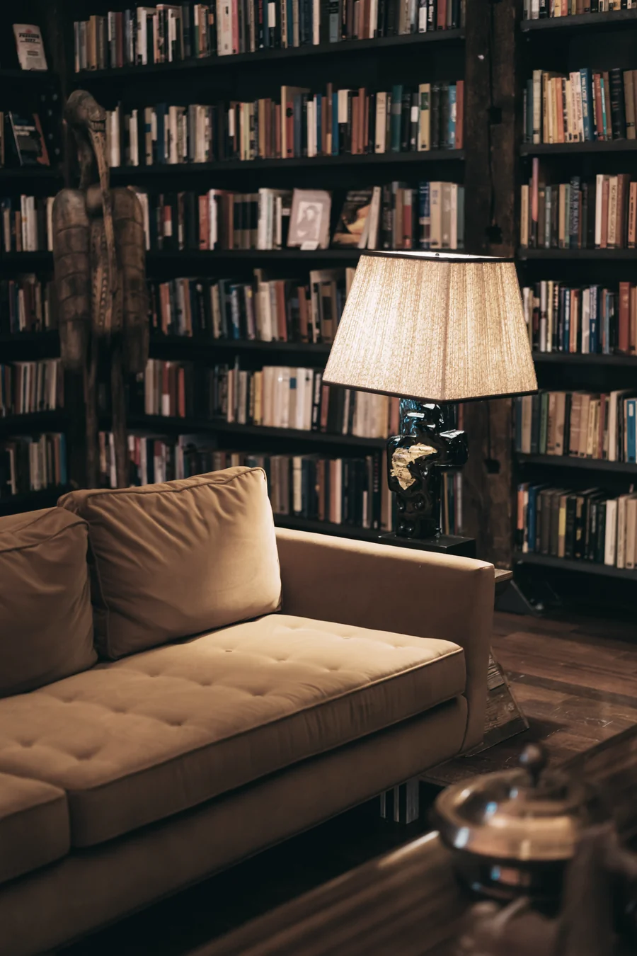 A reading room lined with bookshelves, a lamp lit beside a comfortable sofa.